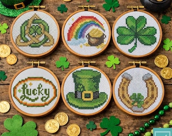Könnte beinhalten: Sechs Stickrahmen mit Kreuzstich-Stickereien zum Thema St. Patrick's Day. Designs umfassen ein Kleeblatt, einen Regenbogen mit Goldtopf, ein Hufeisen, einen Leprechaun-Hut und das Wort "Lucky". Goldmünzen und grüne Kleeblätter sind verstreut.