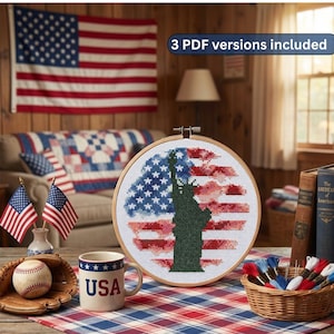 Peut inclure: Un cercle de broderie au point de croix représentant le drapeau américain et la Statue de la Liberté. L'image comprend une balle de baseball, une tasse avec "USA" et de petits drapeaux américains. Le texte "3 PDF versions included" est visible.
