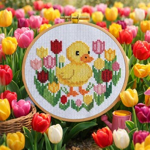 May include: A cross-stitch embroidery hoop featuring a yellow duckling surrounded by colorful tulips. The duckling is the focal point, with a detailed design of a duck and flowers. The hoop is set against a backdrop of a vibrant tulip garden.