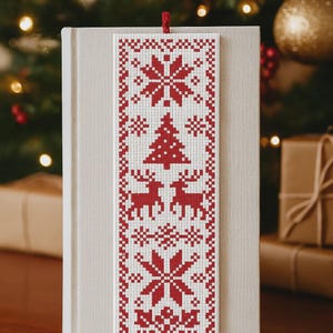 Pode incluir: Marcador de livros de Natal vermelho e branco com um padrão festivo. O design inclui flocos de neve, uma árvore de Natal e renas. O marcador de livros é feito de tecido e tem um borla vermelha.