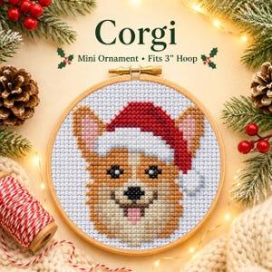 Könnte beinhalten: Eine Kreuzstichstickerei eines Corgi-Hundes mit einer rot-weißen Weihnachtsmütze, zentriert in einem runden Holzrahmen. Der Text darüber lautet Corgi Mini Ornament • Fits 3" Hoop. Das Design besteht aus beigen, weißen und schwarzen Fäden auf weißem Stoff.