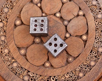 Peut inclure: Deux dés argentés à points rouges reposent sur un plateau de jeu en bois. Le plateau présente un motif circulaire avec des tranches de bois et un anneau extérieur décoratif. Les dés montrent six et cinq points.