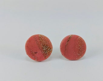 May include: A pair of round stud earrings with a pink base and gold glitter accents.