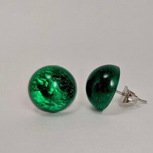 May include: A pair of green resin stud earrings with silver posts. The earrings are round and have a slightly textured surface.