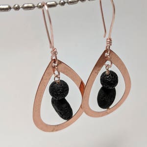 May include: Rose gold teardrop shaped earrings with black lava rock beads hanging from the bottom.