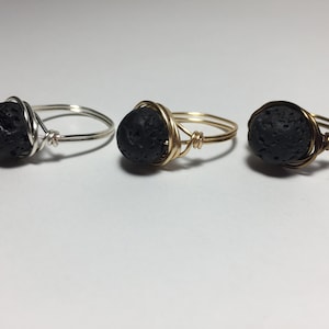 May include: Three rings with black lava rock beads wrapped in wire. The rings are made with silver, gold, and brass wire.