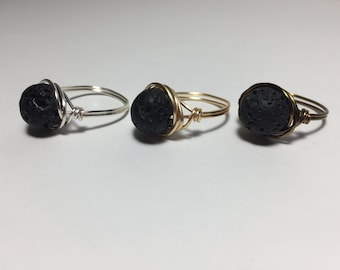 May include: Three rings with black lava rock beads wrapped in wire. The rings are made with silver, gold, and brass wire.