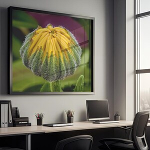 Op de afbeelding: Een ingelijste print van een geel en groene bloemknop hangt boven een bureau in een kantooromgeving. Het bureau heeft een computer, kantoorbenodigdheden en een zwarte stoel. Een groot raam biedt uitzicht op een stadsgezicht.