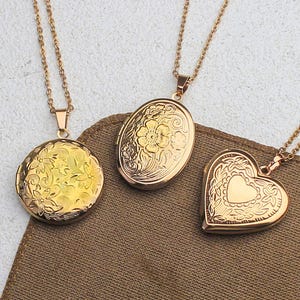 May include: Three gold-colored lockets with delicate floral and heart designs. Each locket hangs from a matching chain. The lockets are round, oval, and heart-shaped, resting on a brown fabric.