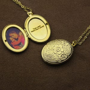 May include: Gold-colored oval locket necklace, one open to reveal a photo and the inscription "Your wick won't burn away." The closed locket features a floral design. The necklace chain is also gold.