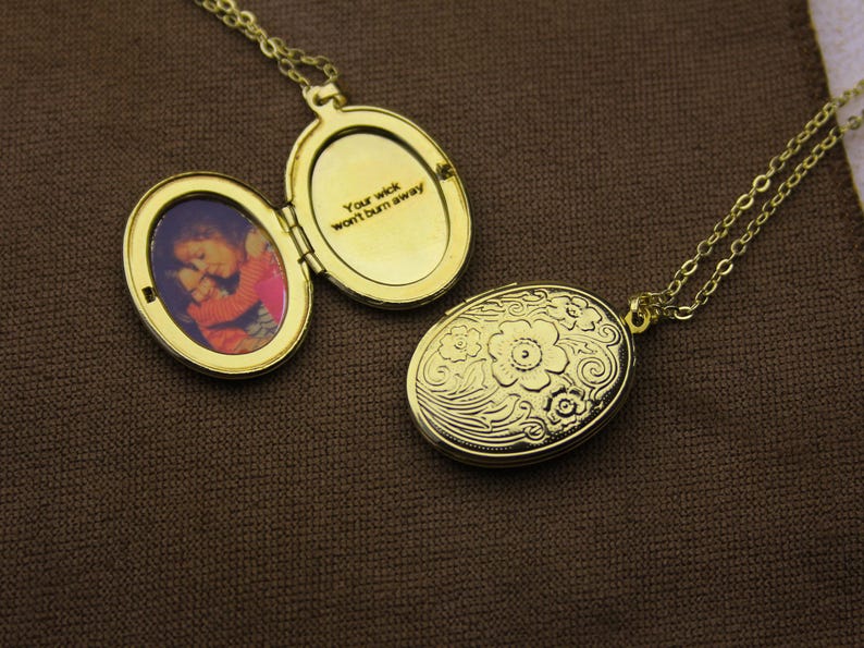 May include: Gold-colored oval locket necklace, one open to reveal a photo and the inscription "Your wick won't burn away." The closed locket features a floral design. The necklace chain is also gold.