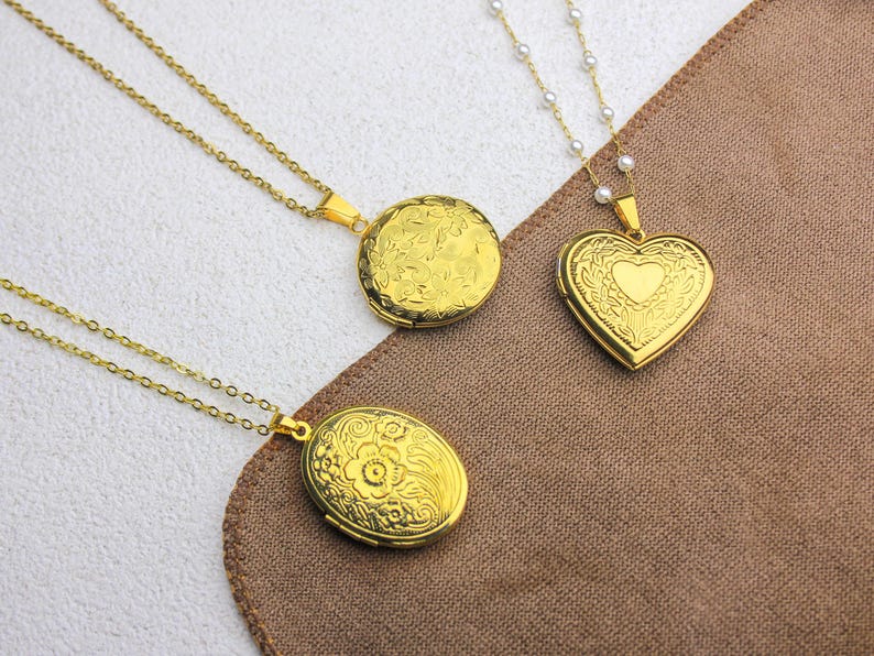 May include: Three gold-colored lockets with intricate floral and heart designs. The lockets are on delicate chains, one with a pearl strand. The lockets are round, oval, and heart-shaped, perfect for holding small photos or keepsakes.