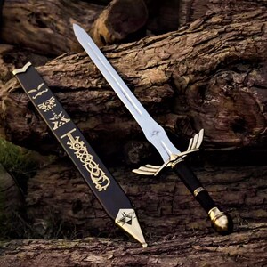 May include: A silver-bladed sword with a gold hilt and black handle rests beside its black sheath. The sheath features gold embellishments and a gold tip. The sword and sheath are displayed on a textured, brown surface.