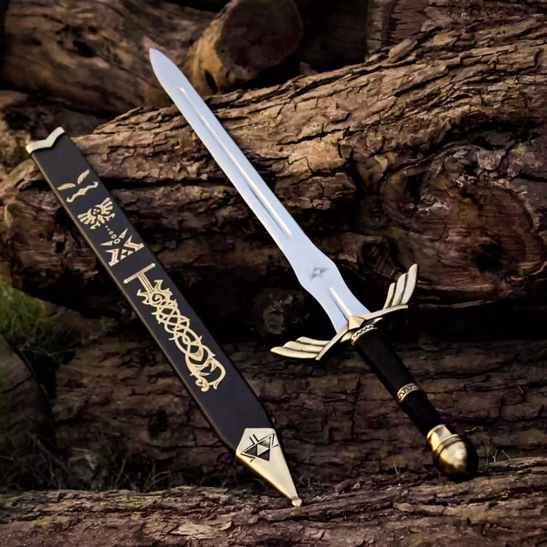 May include: A silver-bladed sword with a gold hilt and black handle rests beside its black sheath. The sheath features gold embellishments and a gold tip. The sword and sheath are displayed on a textured, brown surface.