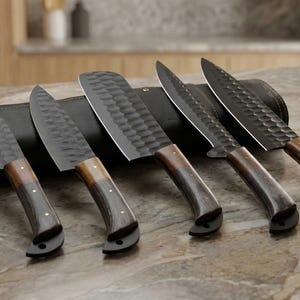 May include: A set of five kitchen knives with dark blades and wooden handles, displayed on a countertop. The blades have a textured pattern, and the handles transition from light to dark brown. A black leather knife roll is behind the knives.