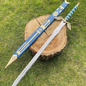 May include: A silver sword with a gold hilt and a blue and gold scabbard. The sword is resting on a wooden surface. The scabbard is blue with gold accents and a gold tip. The handle of the sword is wrapped in blue and green.