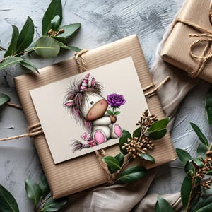 Puede incluir: Una tarjeta de felicitaci&oacute;n con un unicornio de dibujos animados sosteniendo una rosa p&uacute;rpura, colocada sobre un regalo envuelto. El unicornio tiene detalles rosas y marrones. El regalo est&aacute; envuelto en papel marr&oacute;n y atado con hilo, con acentos de follaje verde.