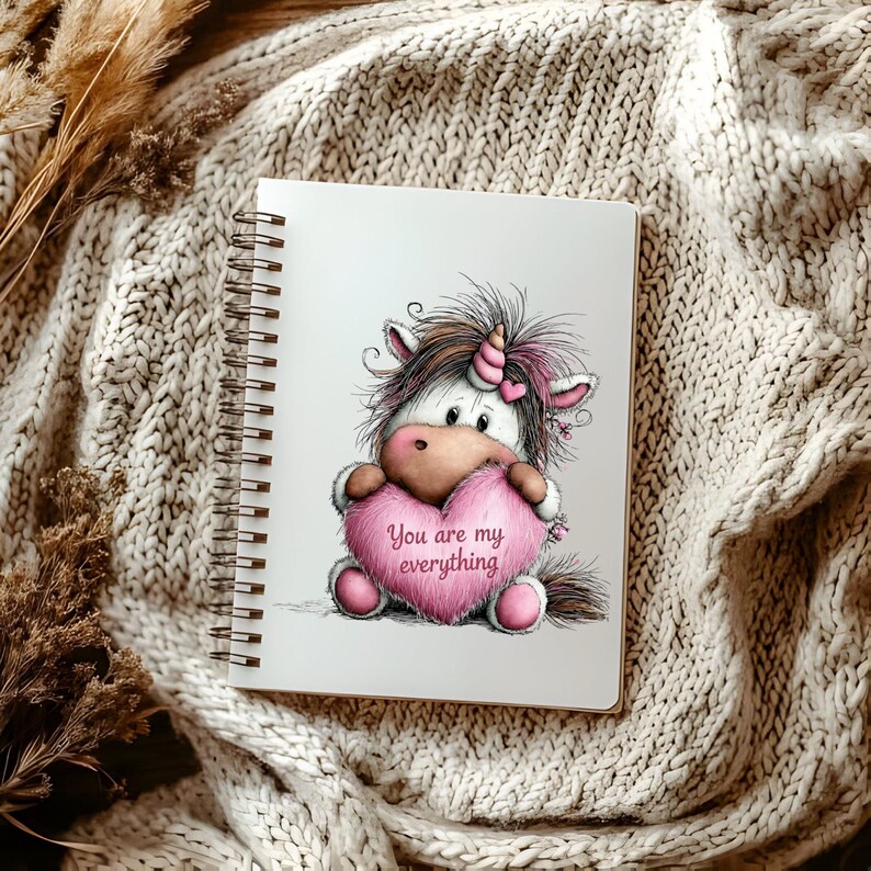Puede incluir: Un cuaderno con espiral con una ilustraci&oacute;n de un unicornio sosteniendo un coraz&oacute;n rosa. El coraz&oacute;n tiene el texto "You are my everything". El unicornio tiene una melena marr&oacute;n y un cuerno rosa, sobre un fondo blanco.
