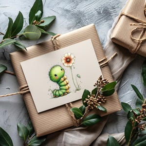 May include: A greeting card featuring a cartoon caterpillar with a flower, resting on a wrapped gift. The card has a light beige background with a green and yellow caterpillar. The gift is wrapped in brown paper and tied with twine, with green foliage accents.