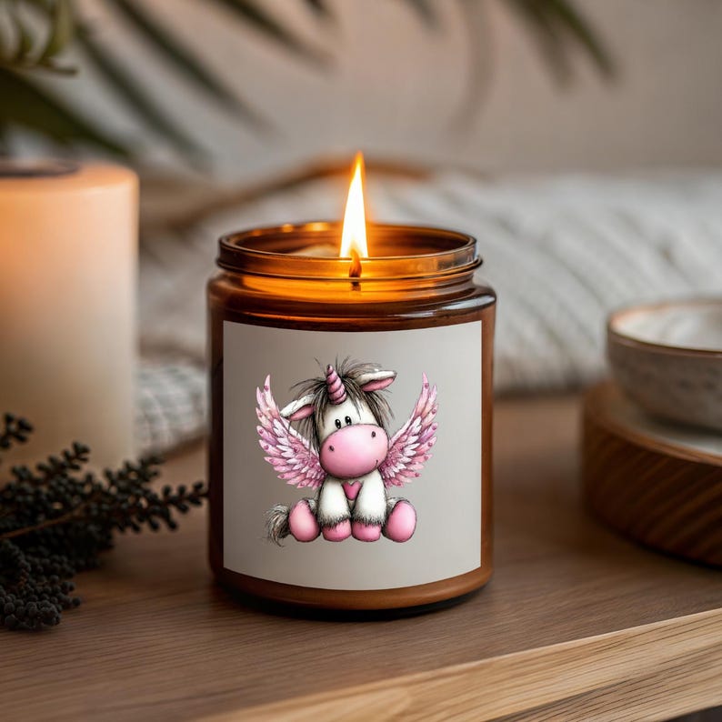 Puede incluir: Una vela encendida en un frasco de vidrio marr&oacute;n con una etiqueta que presenta un unicornio de dibujos animados con alas rosas. El unicornio tiene un coraz&oacute;n rosa. La vela est&aacute; en una bandeja de madera.