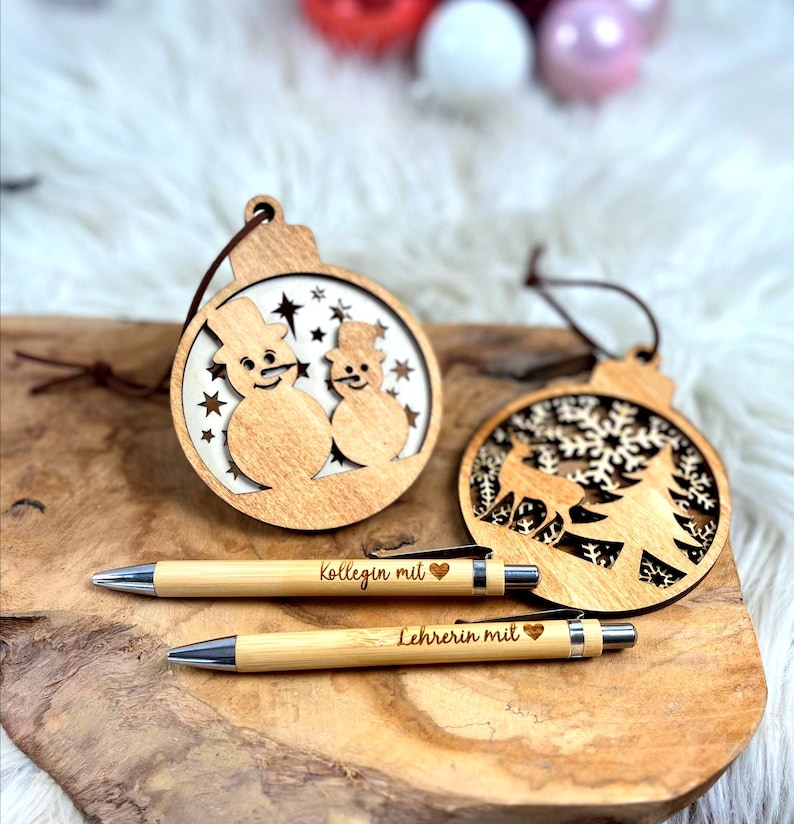Wichtelgeschenk Kollegin, Kugelschreiber als Geschenk mit Gravur, Personalisierte Kulis, Mitarbeiter Geschenke Weihnachten - zwei Kugelschreiber mit der Gravur "Kollegin mit Herz" und "Lehrerin mit Herz" und zwei Weihnachtsanhänger aus Holz mit einem Schneemännermotiv und einem Hirsch mit Tannenbaum Motiv.