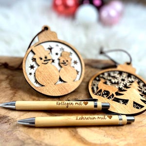 Wichtelgeschenk Kollegin, Kugelschreiber als Geschenk mit Gravur, Personalisierte Kulis, Mitarbeiter Geschenke Weihnachten - zwei Kugelschreiber mit der Gravur "Kollegin mit Herz" und "Lehrerin mit Herz" und zwei Weihnachtsanhänger aus Holz mit einem Schneemännermotiv und einem Hirsch mit Tannenbaum Motiv.
