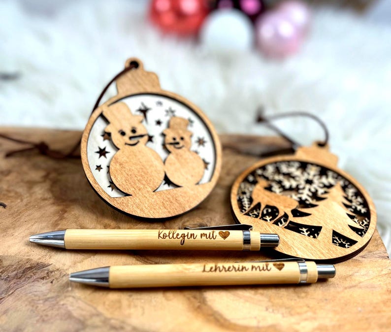 Wichtelgeschenk Kollegin, Kugelschreiber als Geschenk mit Gravur, Personalisierte Kulis, Mitarbeiter Geschenke Weihnachten - zwei Kugelschreiber mit der Gravur "Kollegin mit Herz" und "Lehrerin mit Herz" und zwei Weihnachtsanhänger aus Holz mit einem Schneemännermotiv und einem Hirsch mit Tannenbaum Motiv.