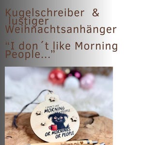May include: A wooden Christmas ornament with a dog illustration and the text "I don't like Morning People... Or Mornings Or People." Two pens are below the ornament. The ornament is hanging on a string.