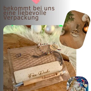 May include: A wooden bookmark and pen set with the words "F&uuml;r Dich Lehrerin mit" engraved on the bookmark. The set is packaged with a small wooden card and a decorative tag. The image also includes text that says "JEDES ST&Uuml;CK bekommt bei uns eine liebevolle Verpackung".