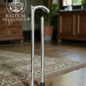 Puede incluir: Un bastón plateado pulido con un mango curvo y un eje texturizado. El bastón está de pie sobre un suelo de madera. El logotipo "Nautical Elegance" es visible en la esquina superior izquierda e inferior derecha.
