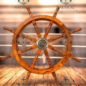 Puede incluir: Un timón de barco de madera con ocho radios y un centro de latón. El timón es de color marrón cálido y se encuentra sobre un fondo de madera borroso. Las palabras "NAUTICAL ELEGANCE" están estampadas en la imagen.