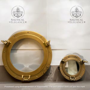 Op de afbeelding: Twee messing patrijspoorten, één groot en één klein, met een helder glazen midden en een cirkelvormig ontwerp. De patrijspoorten hebben een nautisch thema, met de woorden "NAUTICAL ELEGANCE" op de achtergrond.