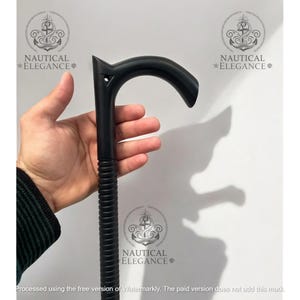 Puede incluir: Un bastón negro con un mango curvo y un eje texturizado. El bastón se sostiene en una mano sobre un fondo blanco. El texto "NAUTICAL ELEGANCE" es visible en la imagen.