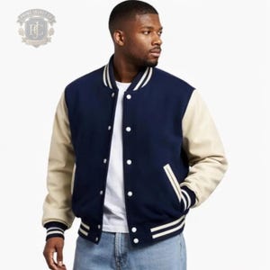 Könnte beinhalten: Eine marineblaue Collegejacke mit cremefarbenen Ärmeln sowie geripptem Kragen, Bündchen und Saum mit weißen Streifen. Die Jacke hat eine Druckknopfleiste, zwei Seitentaschen mit weißer Einfassung und wird über einem weißen T-Shirt getragen.