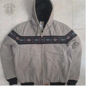 May include: A beige hooded jacket with a full-length front zipper and a black interior lining. A horizontal band across the chest and sleeves features a geometric pattern in red, teal, and white. The jacket includes black ribbed cuffs and hem.