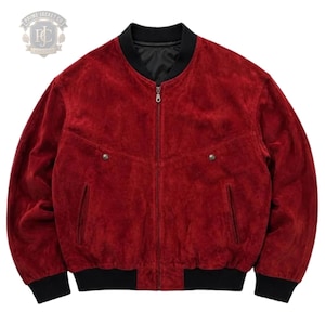 Könnte beinhalten: Eine tiefrote Wildleder-Bomberjacke mit schwarzem Rippstrickkragen, Bündchen und Saum. Die Jacke verfügt über einen zentralen Metallreißverschluss, zwei schräge Seitentaschen und zwei Brusttaschen mit Metalldruckknöpfen. Ein Logo ist oben links sichtbar.