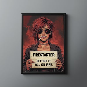 Puede incluir: Impresión artística enmarcada que presenta a una mujer con cabello rojo y gafas de sol, sosteniendo un letrero que dice "Firestarter Setting It All On Fire". La obra de arte tiene un estilo de cómic con una combinación de colores rojo y negro.