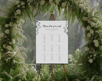 May include: A wedding seating chart on a bronze easel, with the text "Please find your seat". The chart is surrounded by a floral arch of white roses and greenery. The names "Marisela & Matthias" are also visible.