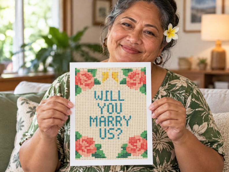 Puede incluir: Una tarjeta rectangular blanca con un patr&oacute;n de punto de cruz pixelado y el texto "WILL YOU MARRY US?" en azul. El dise&ntilde;o incluye cuatro grupos de rosas rosadas con hojas verdes en las esquinas y dos peque&ntilde;as formas amarillas arriba.