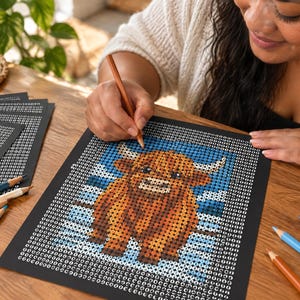 May include: A paint-by-number style coloring sheet featuring a brown Highland cow with long horns against a blue background, printed on black paper with numbered circles, accompanied by several colored pencils on a wooden surface.