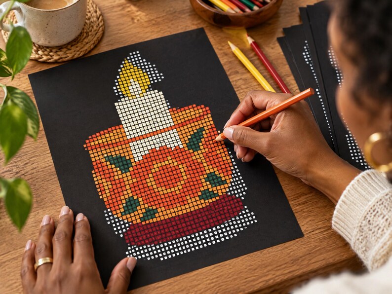 May include: A black sheet of paper featuring a pixel art design of a lit candle in a decorative holder. The candle has a yellow flame and white wax, while the holder is orange with dark green leaf accents and a deep red base.