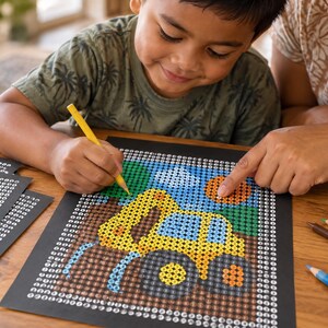 May include: A color-by-number activity sheet featuring a yellow construction excavator on a black background with a grid of numbered circles. The design includes green, blue, and orange elements, with colored pencils scattered on the wooden surface.