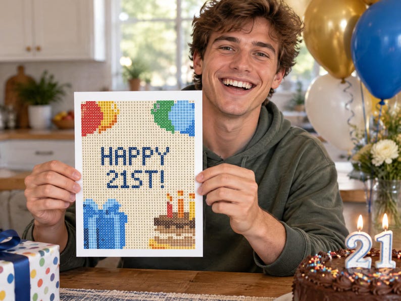 May include: A rectangular diamond painting card featuring a pixelated design with the text HAPPY 21ST! in blue. The card displays colorful balloons, a blue gift box, and a birthday cake with lit candles against a light tan grid background.