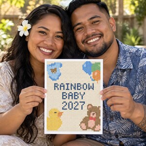 Puede incluir: Un letrero rectangular con un diseño de punto de cruz pixelado con el texto RAINBOW BABY 2027 en azul oscuro. El diseño incluye un body de bebé azul, un grupo de globos coloridos, un patito de goma amarillo y un oso de peluche marrón.