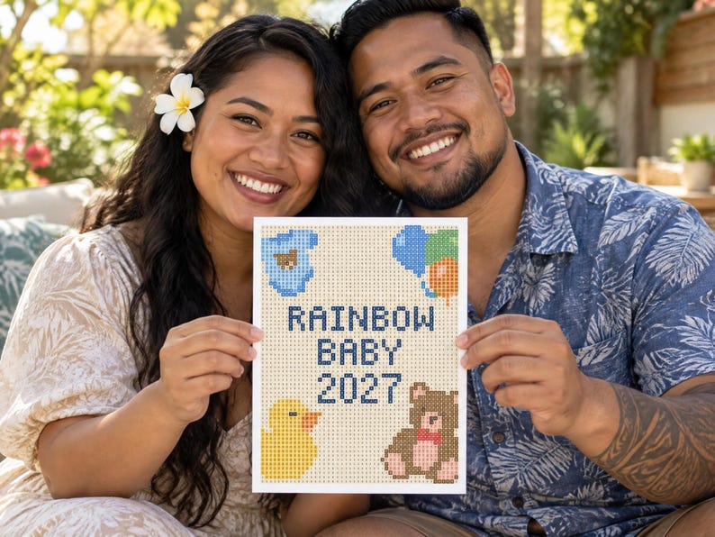 Pu&ograve; includere: Un cartello rettangolare con un design a punto croce pixelato con il testo RAINBOW BABY 2027 in blu scuro. Il design include un body per neonati blu, un gruppo di palloncini colorati, una papera di gomma gialla e un orsacchiotto marrone.