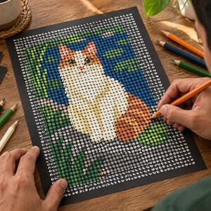 May include: A paint-by-number kit featuring a cat illustration on a black background with a grid of numbered circles. The design includes a white and orange cat surrounded by green foliage and blue water elements, with colored pencils nearby.