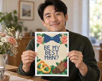 May include: A rectangular cross-stitch pattern on white fabric featuring the text BE MY BEST MAN? in blue, surrounded by a blue bow tie, pink flowers, two gold rings, and a brown dress shoe, all rendered in a pixelated grid design style.
