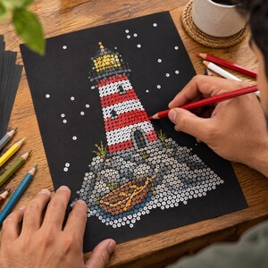 Op de afbeelding: Een zwart vel papier met een illustratie van een vuurtoren bestaande uit genummerde cirkels om in te kleuren. De vuurtoren heeft rode en witte horizontale strepen, een gele top en staat op een rotsachtige basis met een kleine boot.