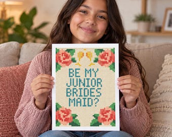 May include: A rectangular print featuring a pixelated design on a light beige background. The text reads BE MY JUNIOR BRIDES MAID? in teal letters. The design is framed by four clusters of pink roses with green leaves and two small yellow glasses.