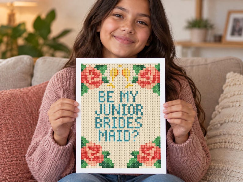 May include: A rectangular print featuring a pixelated design on a light beige background. The text reads BE MY JUNIOR BRIDES MAID? in teal letters. The design is framed by four clusters of pink roses with green leaves and two small yellow glasses.